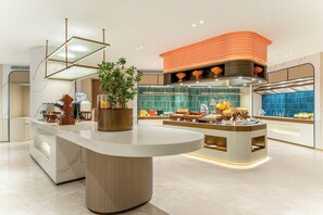 Un moderno vestíbulo de hotel con una recepción central, una planta decorativa y una amplia pared de acento naranja.
