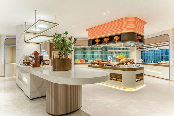 A modern hotel lobby with a central reception desk, a decorative plant, and a large orange accent wall.