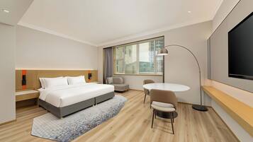 Een moderne hotelkamer met een bed, nachtkastje, stoel, televisie en een groot raam.