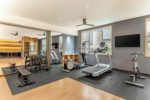 Un gimnasio moderno con equipo de ejercicio, un espejo grande y vistas a la ciudad a través de las ventanas.
