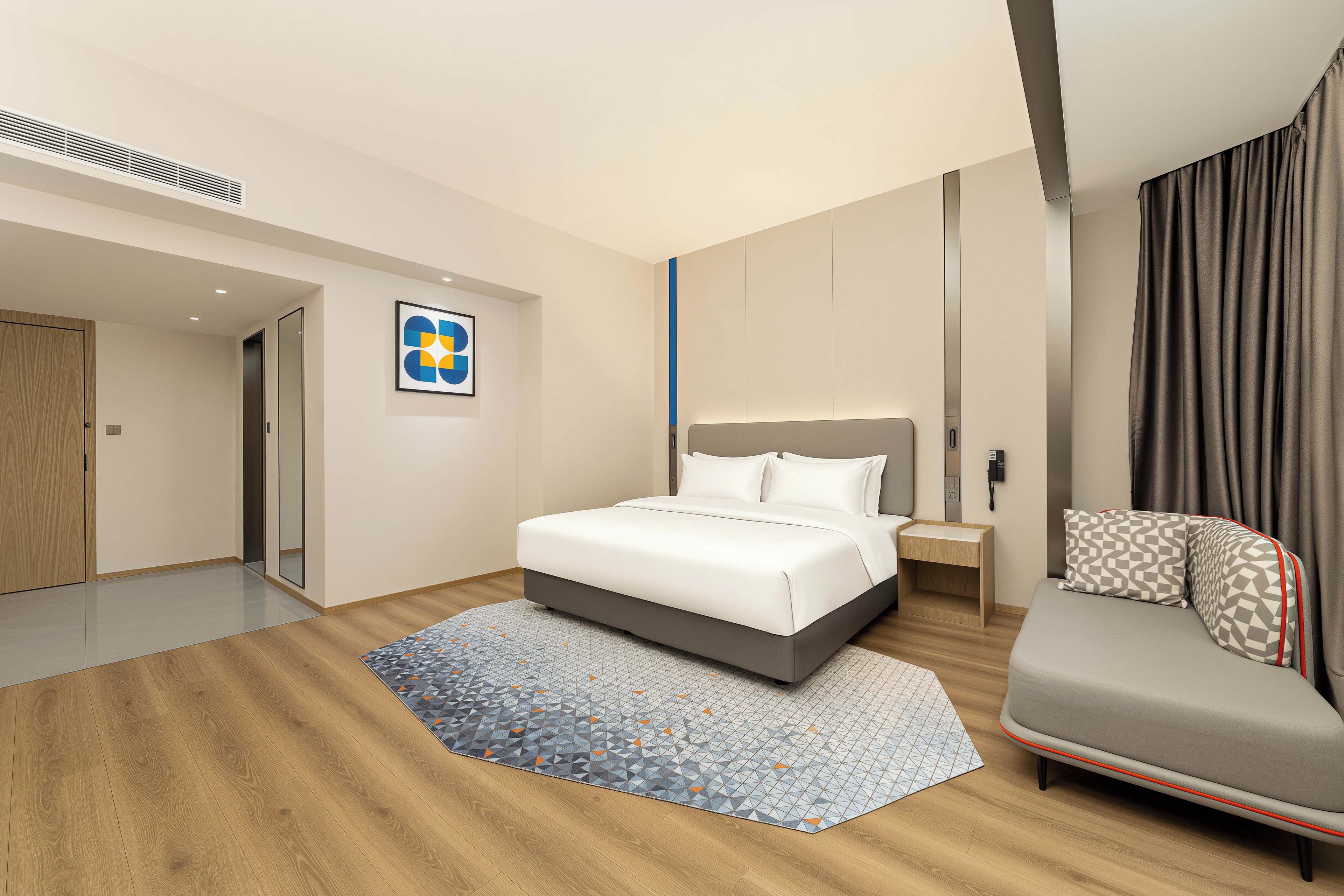 Ein modernes Hotelzimmer mit Bett, Sofa, einem kleinen Nachttisch und einem großen Fenster mit Vorhängen.