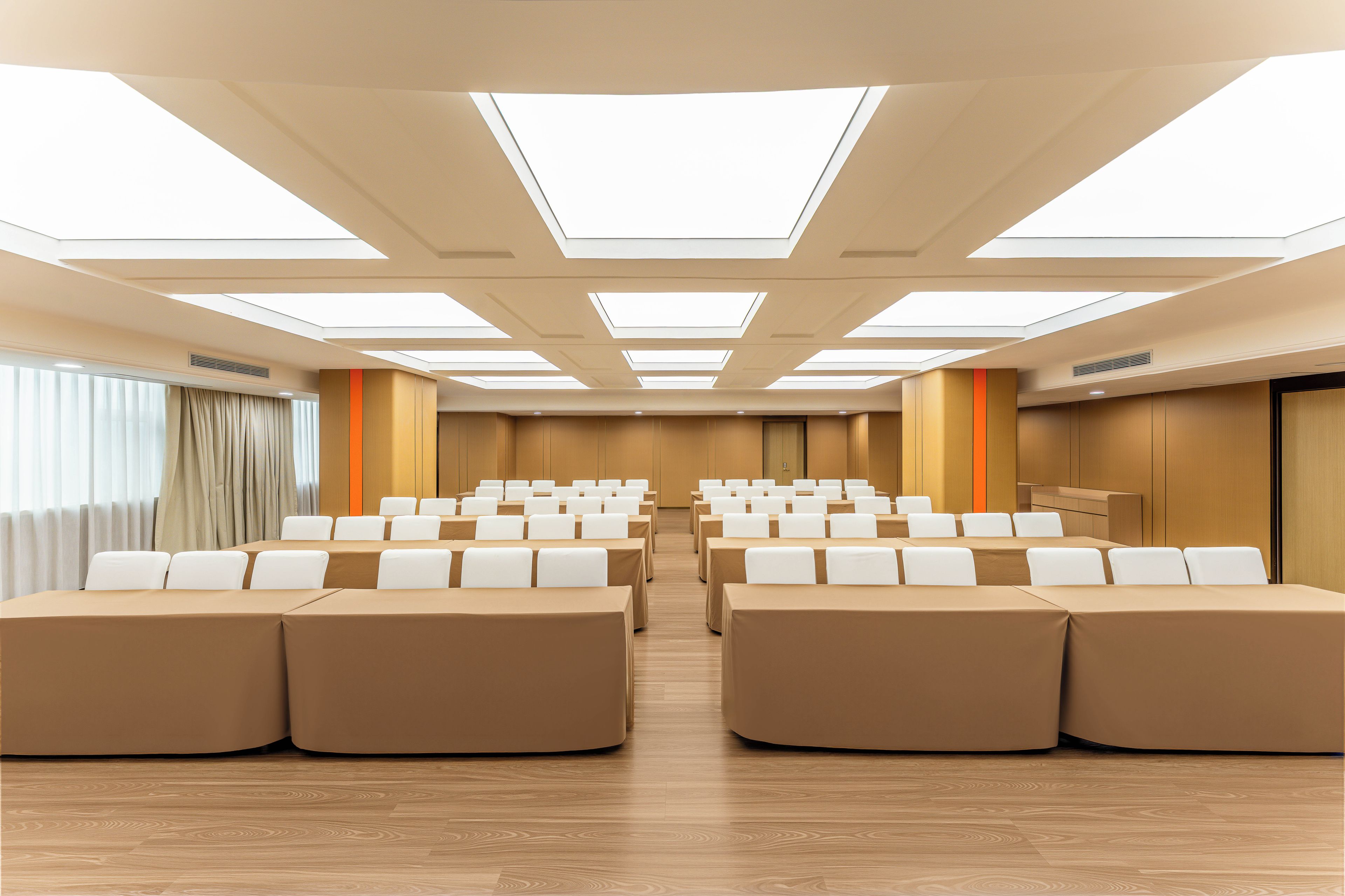 A conference room with rows of tables and chairs, a podium, and a large window with curtains.