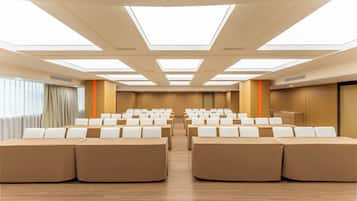 A conference room with rows of tables and chairs, a podium, and a large window with curtains.
