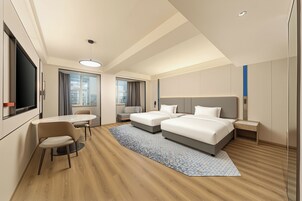 Habitación de hotel con dos camas, un escritorio, una silla, un televisor y un ventanal grande.