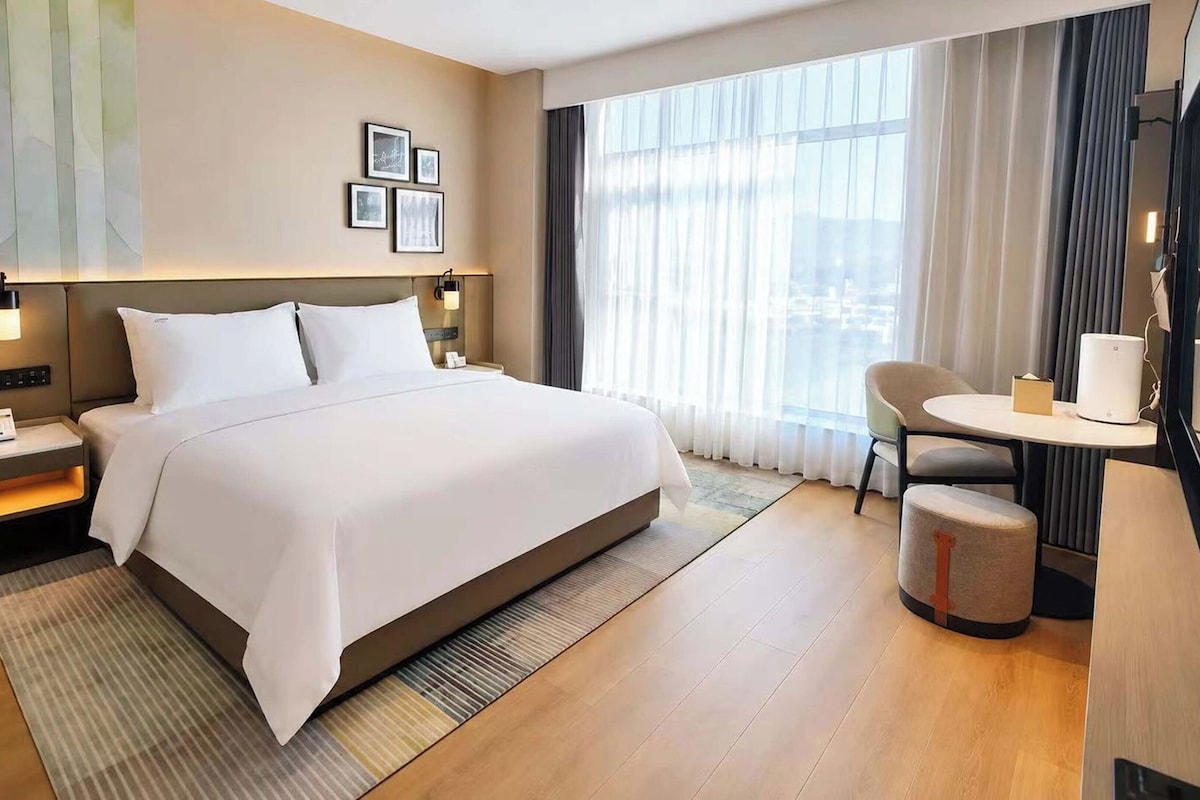 Una habitación de hotel con una cama grande, mesitas de noche, un escritorio y una silla.