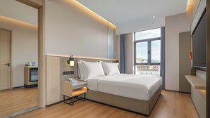 Habitación de hotel moderna con una cama grande, mesita de noche, lámpara y vistas a la ciudad desde la ventana.