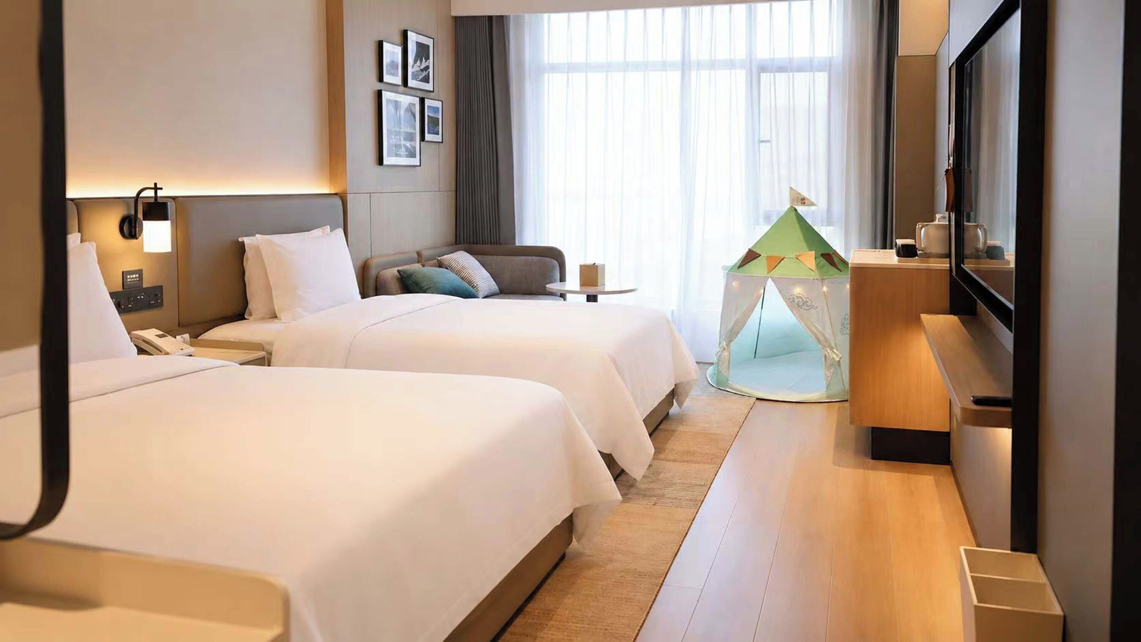 A hotel room with two beds, a small table, a tent-like structure, and a television.