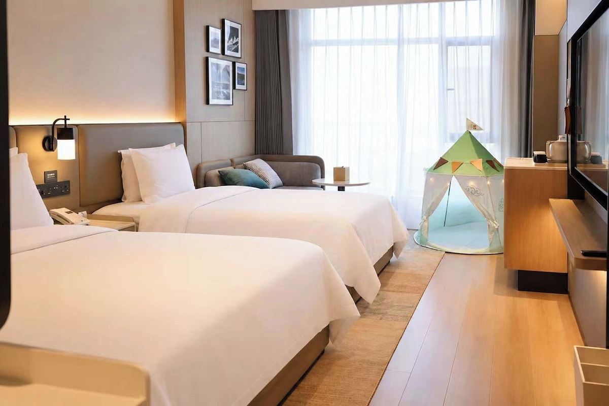 Una habitación de hotel con dos camas, una mesita, una estructura parecida a una tienda de campaña y un televisor.