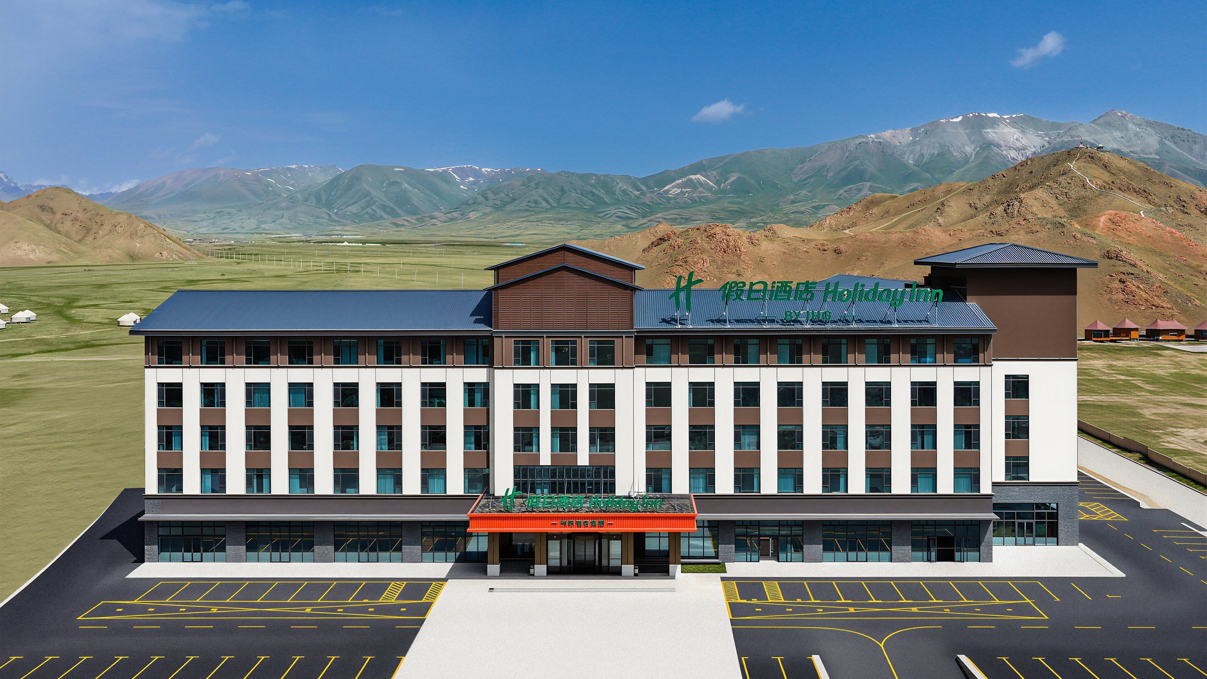 A hotel with a modern design, featuring a large parking lot and a view of mountains in the background.