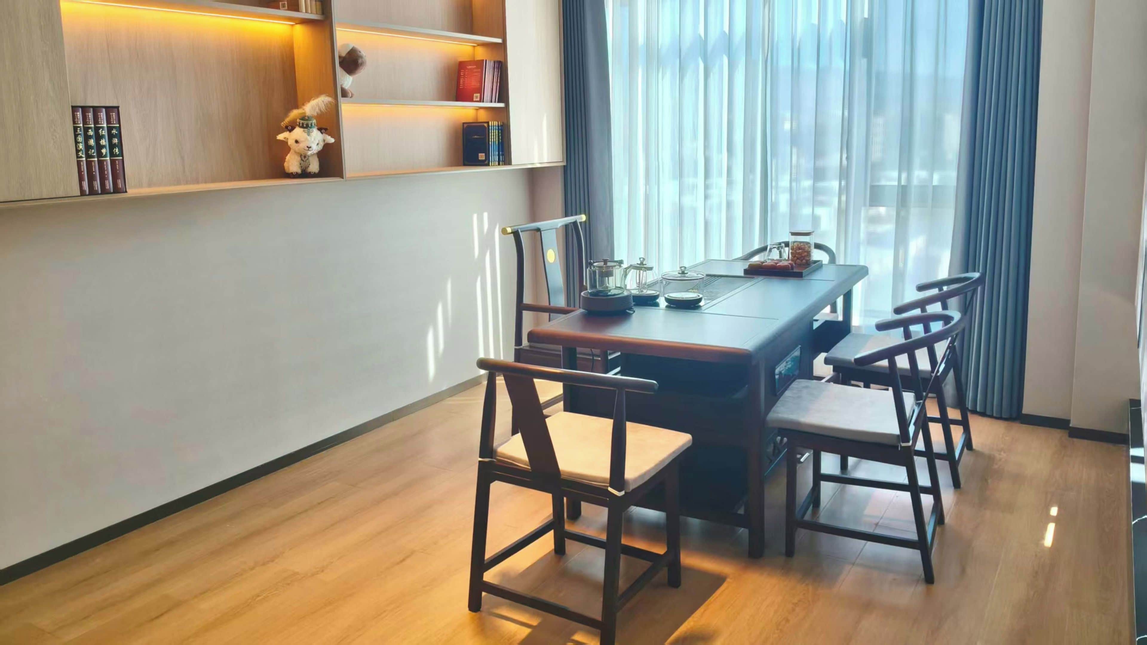 Un coin repas comprenant une table en bois, quatre chaises et une bibliothèque avec des livres et des objets décoratifs.