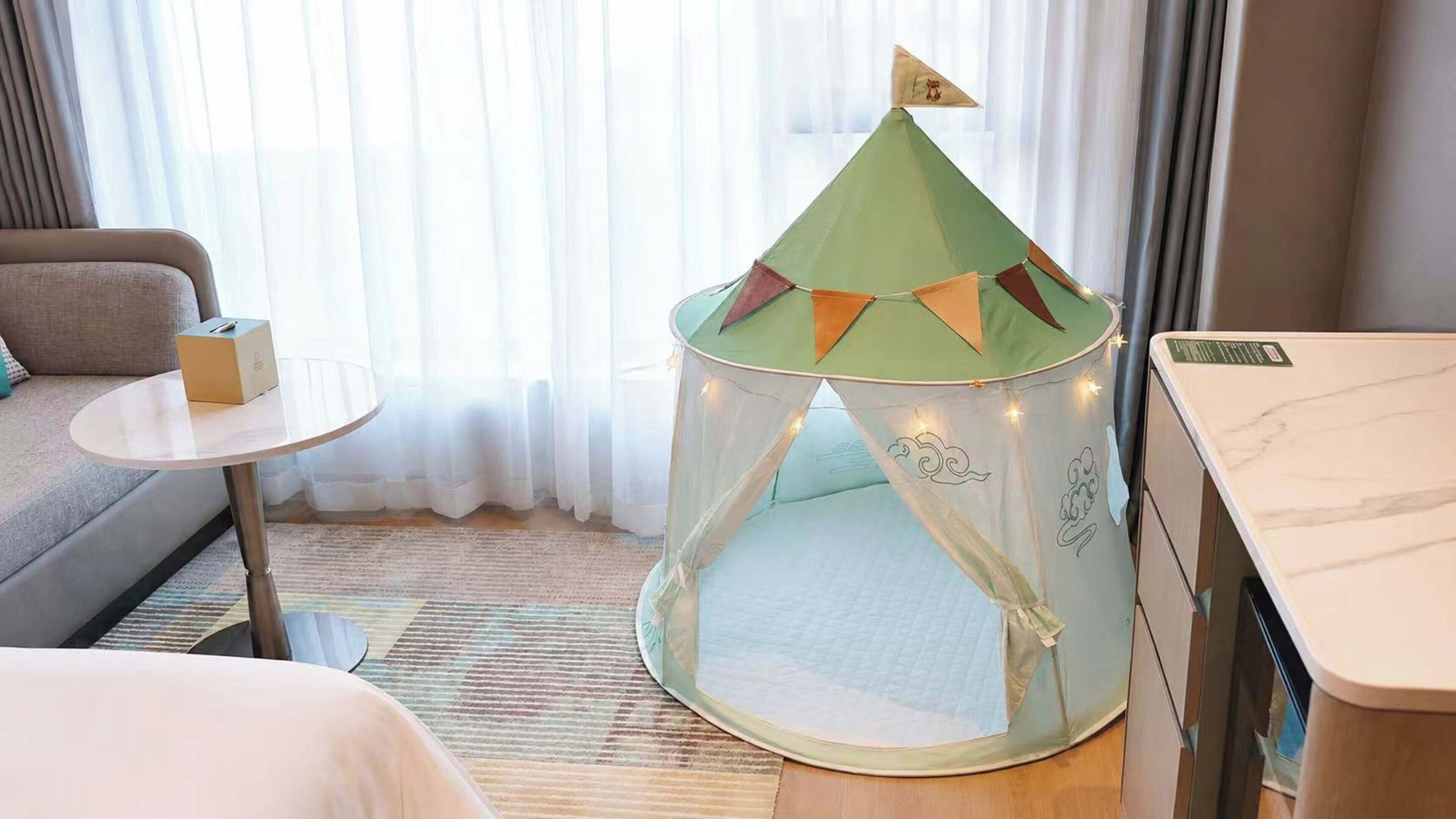 A hotel room with a play tent, a sofa, a small round table, and a bed.