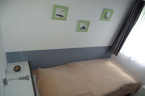A small room with a bed, a nightstand, and three framed pictures on the wall.