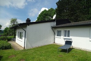 A white house with a satellite dish, a lawn, and a single lounge chair.