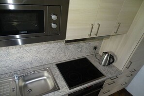 A kitchen with a built-in microwave, a stovetop, a sink, and light wooden cabinets.