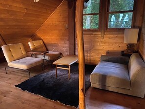 A log cabin interior with a sofa, two armchairs, a small table, and a window with a view of trees. - Private rental type log BASE / Kaga City Ishikawa (Kaga City)