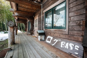 A wooden cabin with a porch, a mailbox, and a window with a view of trees.