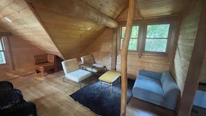 A cozy attic room with a sloped ceiling, a blue sofa, a white chair, a small table, and a wooden bench.