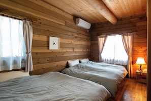 A wooden cabin-style room with two beds, a wall-mounted air conditioner, and a framed picture.