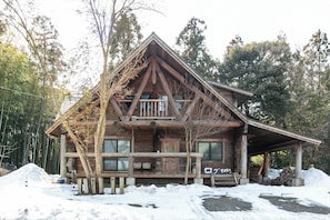 A wooden cabin with a balcony, surrounded by snow and trees.