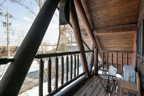 A wooden deck with a railing, a table, and a chair.