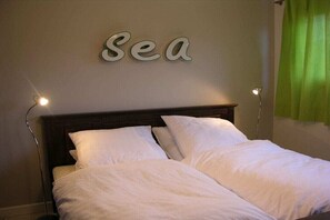 Ein Bett mit weißer Bettwäsche, einem Holz-Kopfstück und einem an der Wand befestigten Schild mit der Aufschrift 'Sea'.