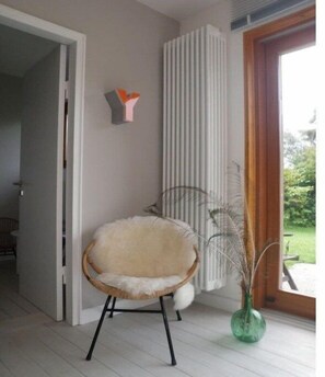 Ein Zimmer mit einem weißen Stuhl, einem Heizkörper, einer grünen Vase und einer Tür zu einem anderen Raum.