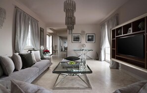 Ein modernes Wohnzimmer mit einer Couch, einem Glastisch und einem Fernseher rechts.