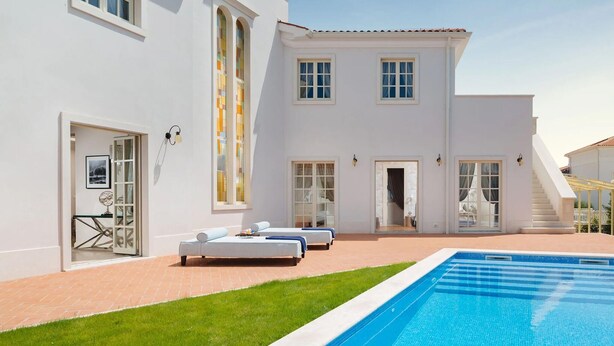 Um edifício branco com piscina, área de estar externa e escadaria que leva a um segundo andar.