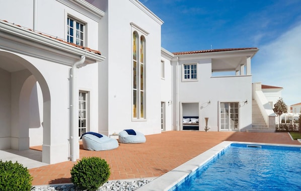 Ein weißes Gebäude mit Swimmingpool, zwei Sitzsäcken und einem kleinen Garten.