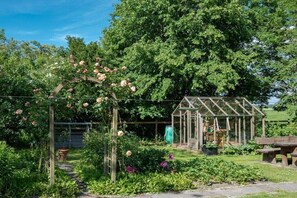 Ein Garten mit einem hölzernen Pergola, einem Gewächshaus und einer Steinsitzbank.