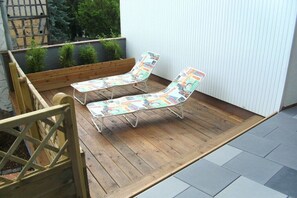 Eine Holzterrasse mit zwei Liegestühlen und einem kleinen Tisch.
