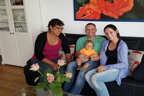 En familie sidder på en sofa med en blomstervase, et skab med glas og et billede på væggen.