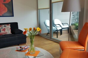 En moderne stue med sofa, lænestol, et glasbord med snacks og en vase med blomster.