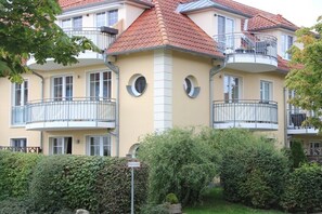 A multi-story building with balconies, a central column, and a well-maintained garden.