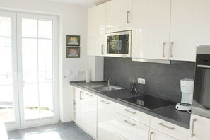A modern kitchen with white cabinets, a black countertop, a built-in microwave, and a coffee maker.