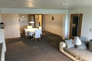 Ein Wohnzimmer mit einer Couch, einem Esstisch und einer Küche im Hintergrund.