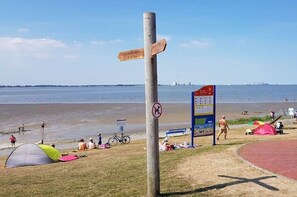 Ein Strand mit einem hölzernen Wegweiser, einem Zelt und einem Spielplatz.