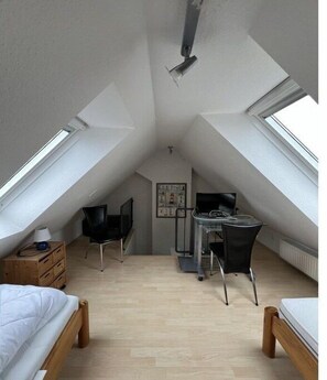 Ein Schlafzimmer im Dachgeschoss mit hohen Decken, Dachfenstern, einem Schreibtisch, zwei Stühlen und einem Bett.