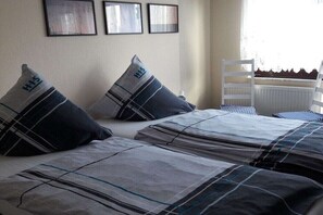 Ein Hotelzimmer mit zwei Betten, gestreifter Bettwäsche, einem weißen Stuhl und gerahmten Bildern an der Wand.
