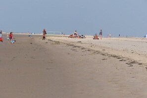 Ein Strand mit Menschen, einige in Badeanzügen, und Strandausstattung wie Liegen und Sonnenschirme.