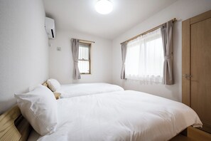 Ein Zimmer mit zwei Betten, einem Fenster mit Vorhängen, einem Holzschrank und einer Deckenleuchte.