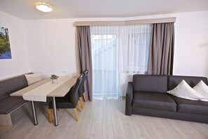Ein modernes Wohnzimmer mit einer Couch, einem Esstisch mit Stühlen und einem Fenster mit Vorhängen.