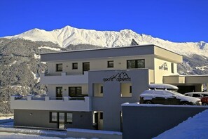 Ein modernes, mehrstöckiges Gebäude vor der Kulisse eines Skigebiets, mit einem gut sichtbaren Logo an der Fassade.