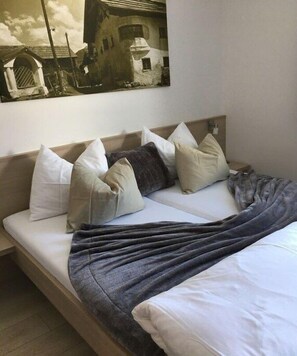 Ein Bett mit grauer Decke, mehreren Kissen und einem Wandbild.