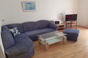 A living room with a sofa, ottoman, glass coffee table, television, and a small white cabinet. - 2 Dissinger Rosi "Valerie" (St. Kanzian)