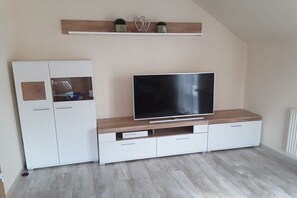 Ein modernes Wohnzimmer mit Fernseher, weißen Schränken und einem Holzregal darüber.