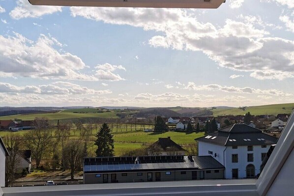 Blick aus einem Fenster auf eine ländliche Landschaft mit Häusern, einer Straße und einem Gebäude mit Solaranlage.