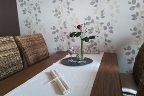 Ein Esstisch mit weißer Tischdecke, einer Vase mit einer roten Rose und einem Glas Wasser.