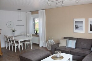 A living room with a dining table, grey sofa, and a white coffee table. - Holiday home in Hage with swimming pool (Hage)