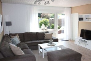 A living room with a sofa, a coffee table, a TV stand, and a window with a view of the outdoors. - Holiday home in Hage with swimming pool (Hage)